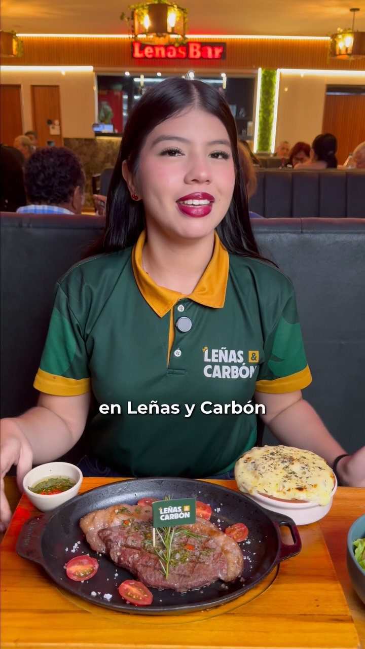 Presentadora con uniforme verde y amarillo, junto a un plato en Leñas y Carbón